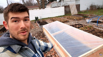 A man with a newly constructed DIY cold frame in his garden.