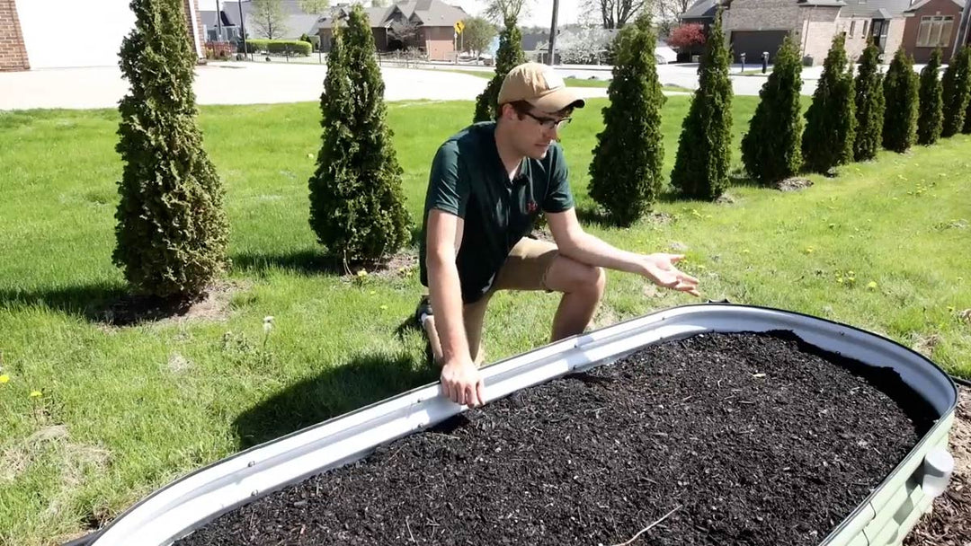 A man gesturing to a newly filled raised garden bed.