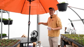 A man standing in a greenhouse next to a heater.