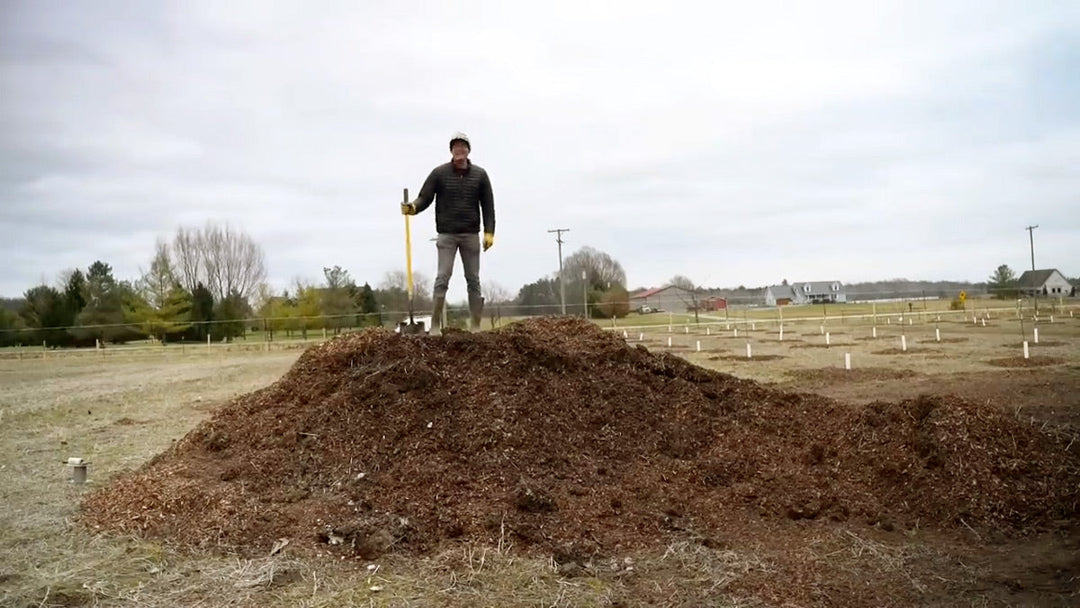 A man standing on a large pile of wood mulch.