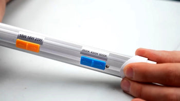 A man holding a grow light with sliders to adjust wattage and Kelvins.